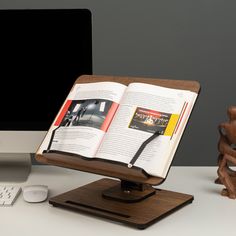 an open book sitting on top of a wooden stand next to a computer keyboard and mouse