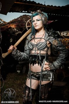 a woman dressed as a warrior holding a baseball bat and wearing leather clothes with chains around her waist