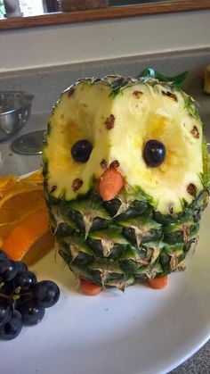 a pineapple shaped like an owl sitting on top of a white plate next to fruit