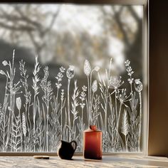 a vase and cup sitting on a table in front of a frosted glass window