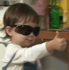 a small child wearing sunglasses and pointing at something on the shelf in front of him