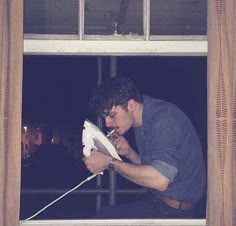 a man is looking out the window while holding an ironing board