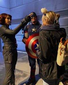 two women dressed up as captain america and black widow are talking to one another on the sidewalk