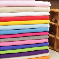 a stack of folded towels sitting on top of a wooden shelf next to a bookcase