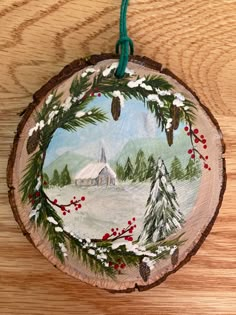 a christmas ornament hanging on a wood slice with pine trees and a church in the background