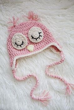 a pink crocheted owl hat with eyes closed on a white furry surface,