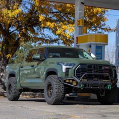 a green truck is parked in front of a gas station with no one around it