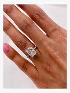 a woman's hand with a diamond ring on top of her finger and the other hand holding an engagement ring