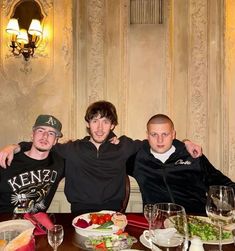 three men sitting at a table with plates of food