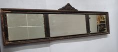 an old mirror hanging on the wall in front of a white wall with black trim