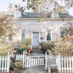 a white picket fence in front of a brick house with potted plants on it