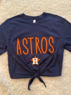 Wear this new Houston Astros game day tee to your next watching party!  The tee is cut to a longer crop and front ties are added. This crop with front ties is one of my best sellers in my shop.  You can choose at check out to have it cut like the picture which is crop with front ties , or crop, which is cut straight across, or have the hem left alone for an original hem. Anyway will be so cute because the font of the Astros is the latest trend. Bella Canvas tee, 100% cotton. Soft and light weight. Machine wash inside out, line dry. If you would like to add something to the tee to personalize it, please let me know. Astros Baseball Game Outfit, Astros Game Outfit, Astros Game Outfit Women, Astros Outfit Woman, Diy Astros Shirt, Houston Astros Outfit, Astros Shirt Ideas, Astros Shirts Vinyl Women, Astros Sweatshirt