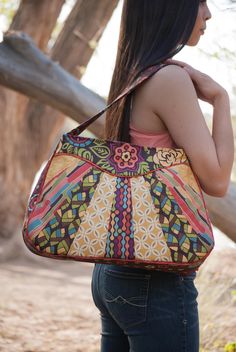 a woman carrying a multicolored handbag on her back while standing in the woods