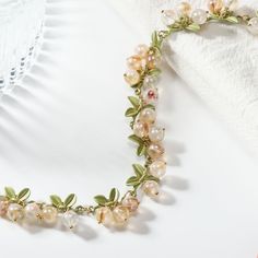 a close up of a necklace with flowers and leaves on the neckline next to a glass vase