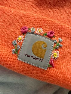 an orange beanie with flowers on it and the word carniflt written in white