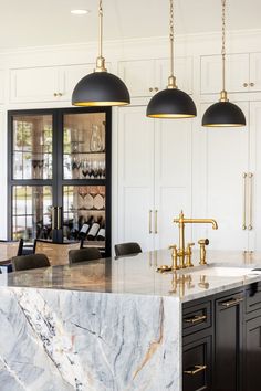 a large kitchen with marble counter tops and black cabinets, hanging lights above the island