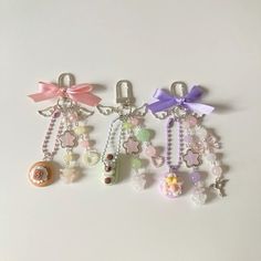 three key chains with charms attached to them on a white surface, one has a pink bow and the other is a purple ribbon