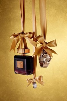 an assortment of perfumes hanging from ribbons on a gold background with a watch in the foreground