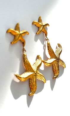 Dive into seaside charm with the "Starfish Earrings" – a delightful pair featuring a larger starfish dangling from a smaller one, both in radiant gold. These earrings capture the whimsy of the ocean, adding a playful touch to your style. Embrace the coastal allure with this charming accessory that evokes the beauty of starfish by the shore. 18k Gold Plated Nickel Free & Hypoallergenic Gold Elegant Earrings With Starfish Charm, Elegant Gold Earrings With Starfish Charm, Yellow Gold Starfish Earrings For Gift, Ocean-inspired Starfish Charm Earrings, Yellow Gold Starfish Earrings With Starfish Charm, Ocean-inspired Drop Earrings With Starfish Charm, Star Charm Drop Earrings For Beach, Ocean-inspired Starfish Charm Dangle Earrings, Ocean-inspired Star Earrings For The Beach