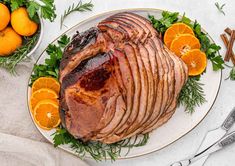 a large ham is on a plate with oranges and parsley around the edges