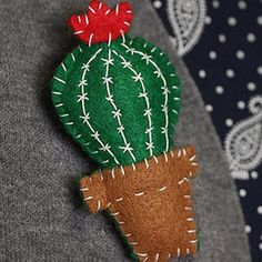 a green cactus brooch sitting on top of a gray sweater