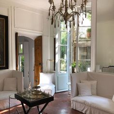 a living room filled with white furniture and a chandelier hanging from the ceiling