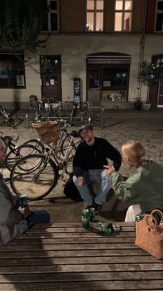 three people sitting on a bench talking to each other in front of bicycles and buildings