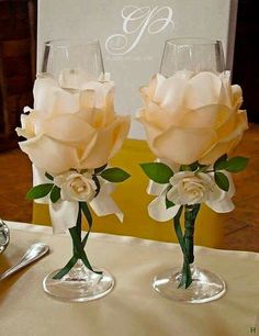 two wine glasses with flowers in them sitting on top of a table next to each other