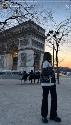 a woman is standing in front of the arc de trioe at sunset with her back to the camera