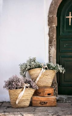 three baskets with flowers sit on the ground in front of a door