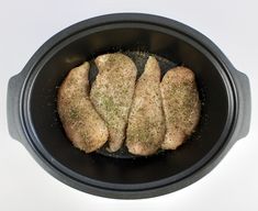 three pieces of meat in a black pan with seasoning on top, ready to be cooked