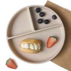 a white plate topped with a sandwich and two strawberries next to a bagel