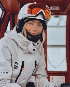 a woman sitting in the back of a ski lift wearing goggles and snow gear