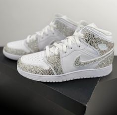 ** PLEASE PLACE YOUR SHOE SIZE IN THE PERSONALIZATION BOX  Where luxury meets style with our custom rhinestoned Nike Air Jordan 1 sneakers, elevate your footwear game with our meticulously crafted designs, blending iconic streetwear with dazzling sophistication. Each pair is meticulously adorned with premium rhinestones, creating a striking statement piece that exudes unparalleled elegance. Whether you're a sneaker aficionado or a fashion-forward trendsetter, our unique creations promise to elevate your look with unmatched flair. Step into the extraordinary and make a lasting impression with our custom rhinestoned Nike Air Jordan 1 sneakers. Luxury Custom Sneakers With Rhinestones And Round Toe, Luxury High-top Sneakers With Rhinestones, Luxury White Sneakers With Rhinestones, High-top Bling Sneakers For Streetwear, Silver High-top Sneakers With Bling, Luxury White Custom Sneakers With Rhinestones, Sporty Bling Sneakers For Streetwear, Sporty Streetwear Sneakers With Bling, White Custom Sneakers With Rhinestones For Streetwear