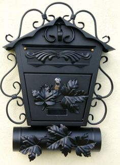 a black mailbox mounted to the side of a building with leaves and acorns on it