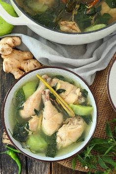 two bowls filled with soup on top of a wooden table next to vegetables and chopsticks