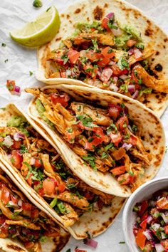 three tortillas with chicken, tomatoes and cilantro on a white table