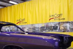 an old purple car parked in front of a yellow wall with the word anncraft on it