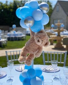 a teddy bear hanging from a bunch of balloons on top of a blue table cloth