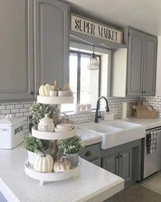 a kitchen with gray cabinets and white counter tops, two tiered trays on the sink