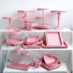 a table topped with lots of pink plates and trays on top of a white table cloth