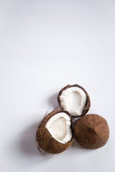 three whole coconuts sitting next to each other on a white surface with one cut in half