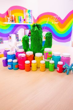 there are many different colored paints on the table and in front of them is a fake cactus