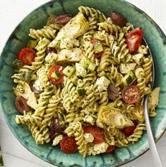 a green bowl filled with pasta salad on top of a white table next to a fork