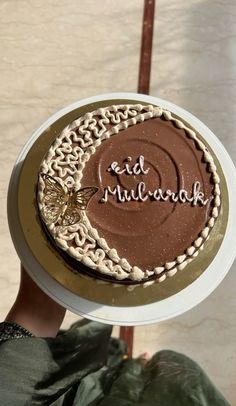 a person holding up a chocolate cake with writing on the top and frosting around it