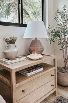 a table with a lamp on it next to a potted plant and a book