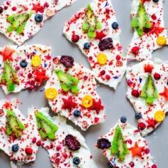 decorated cookies with white frosting and colorful toppings are arranged on a baking sheet