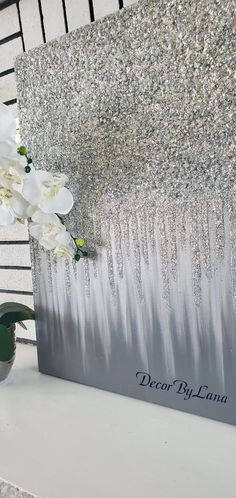 a vase with white flowers sitting on top of a table next to a silver wall