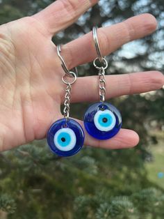 a hand holding two blue evil eye earrings