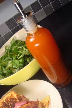 a plate with a sandwich on it next to a bowl of salad and a bottle of ketchup